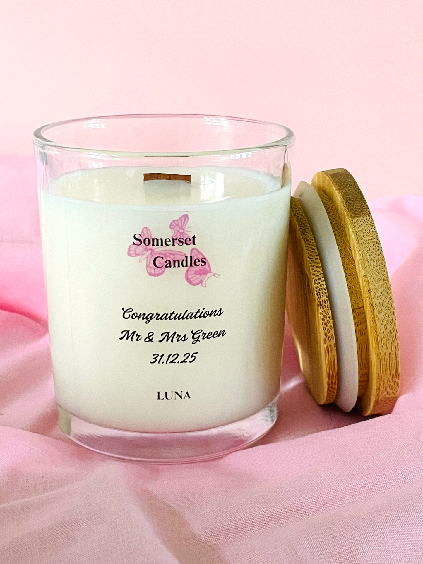 Glass candle with wooden lid on a pink background, featuring 'Somerset Candles' branding.