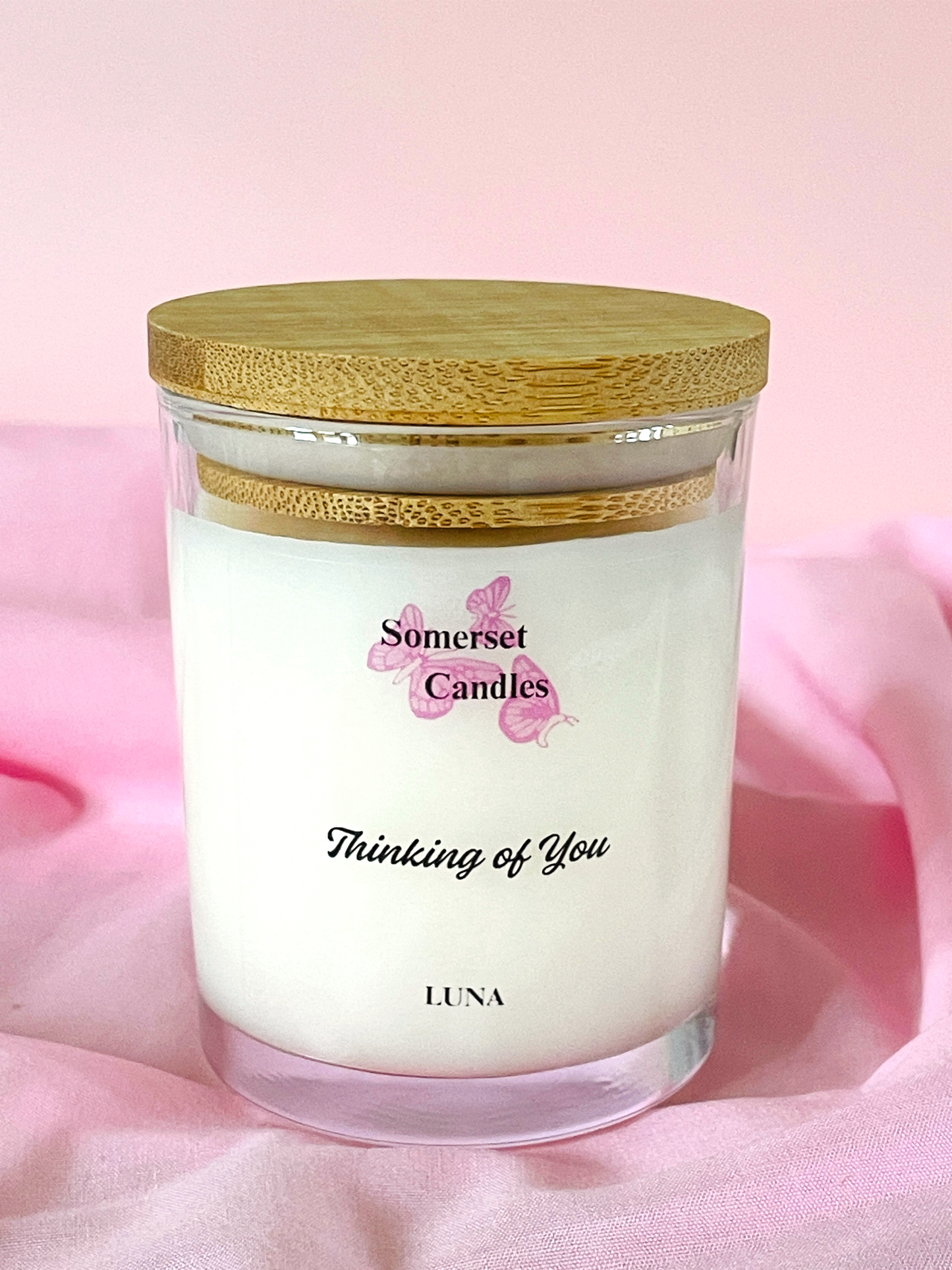Candle in a glass jar with a wooden lid on a pink background, featuring 'Somerset Candles' branding.