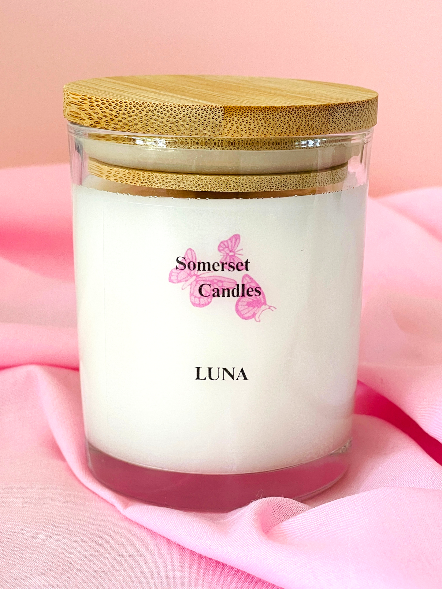 Somerset Candles Luna candle with a wooden lid on a pink fabric background