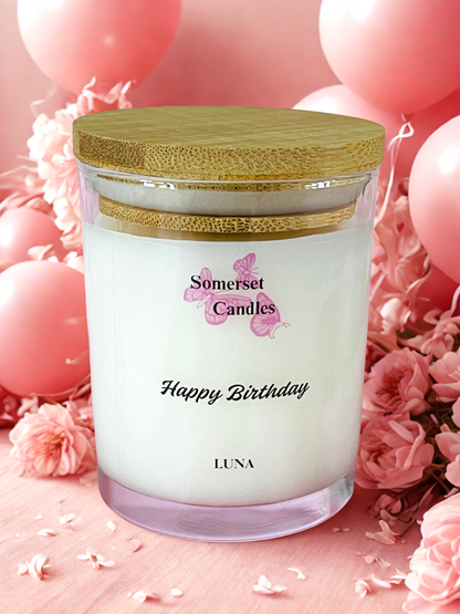 Somerset Candles 'Happy Birthday Luna' candle with pink balloons and flowers in the background