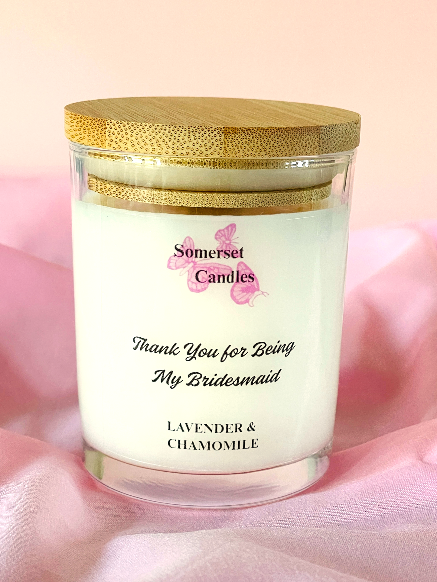 Candle in a 7oz glass jar with a wooden lid on a pink fabric background, featuring 'Somerset Candles' branding.
