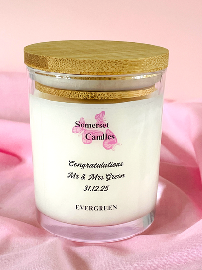 Candle in a glass jar with a wooden lid on a pink fabric background, featuring 'Somerset Candles' branding.