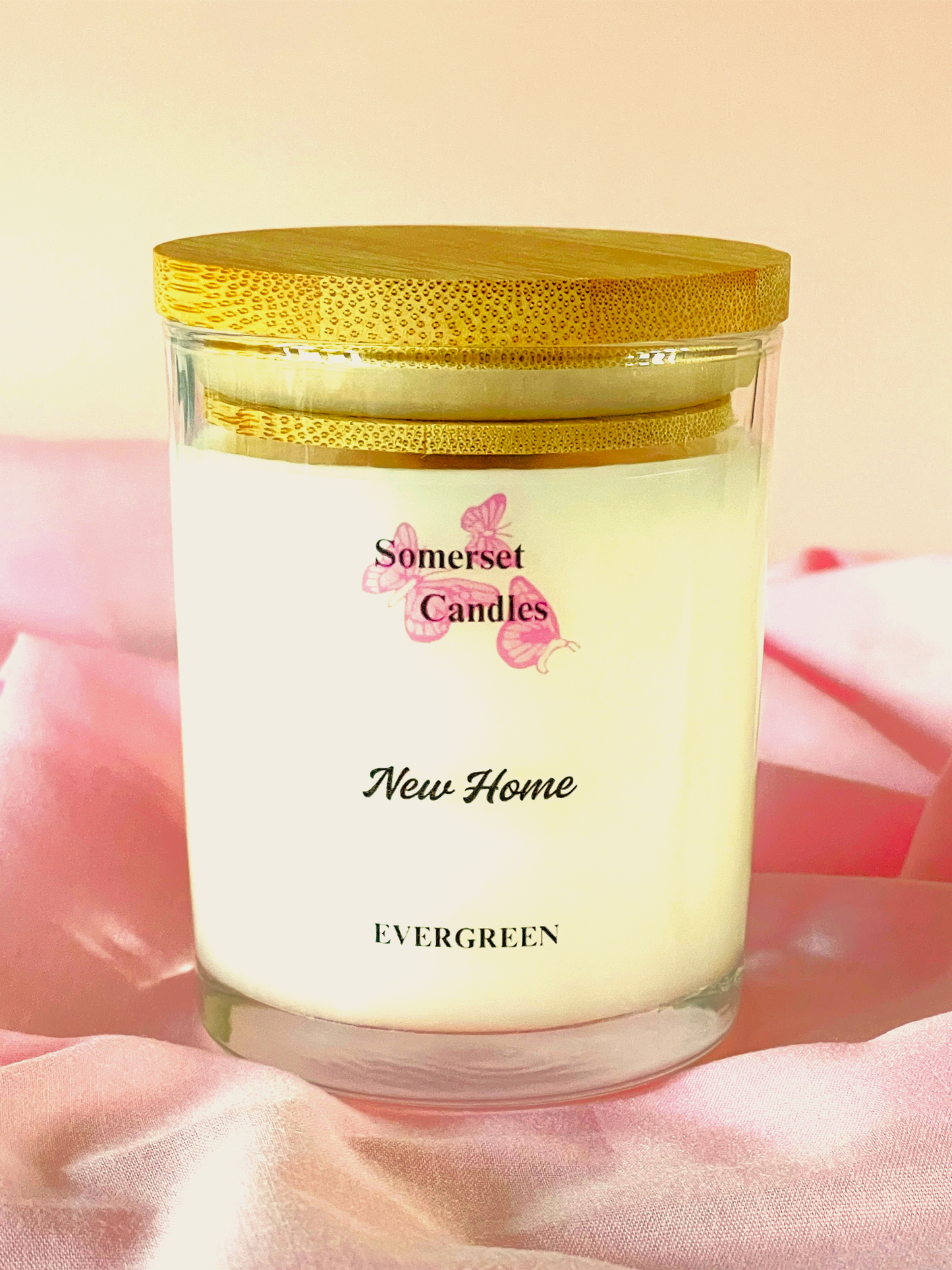 Somerset Candles New Home Evergreen candle with a gold lid on a pink fabric background