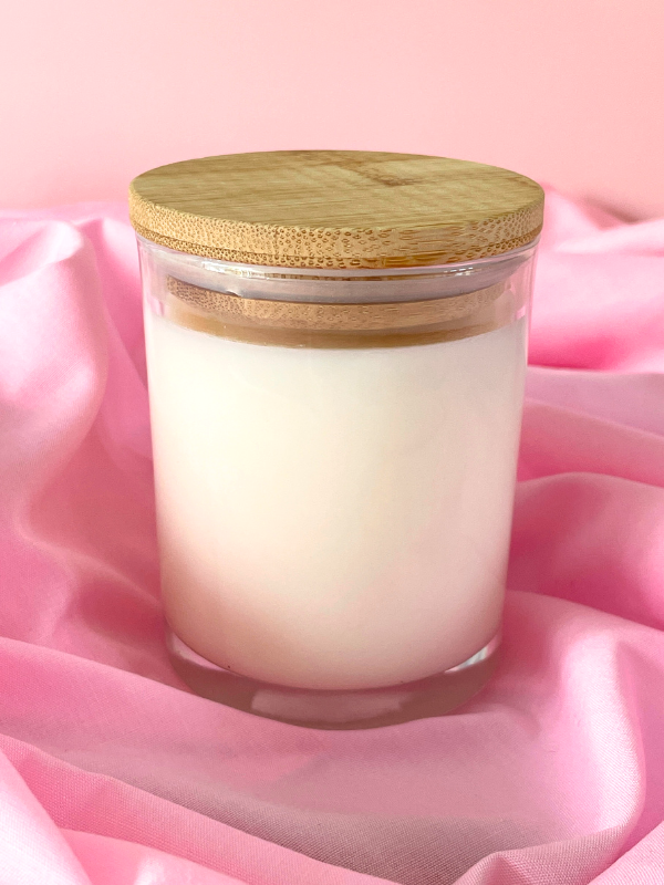 White candle in a glass jar with a wooden lid on pink fabric