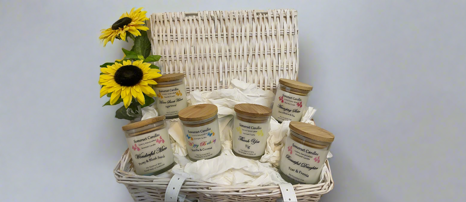 Occasions Candles Collection. One of every scented occasion candle arranged in a wicker basket. There are 2 sunflower to the left hand side of the basket.