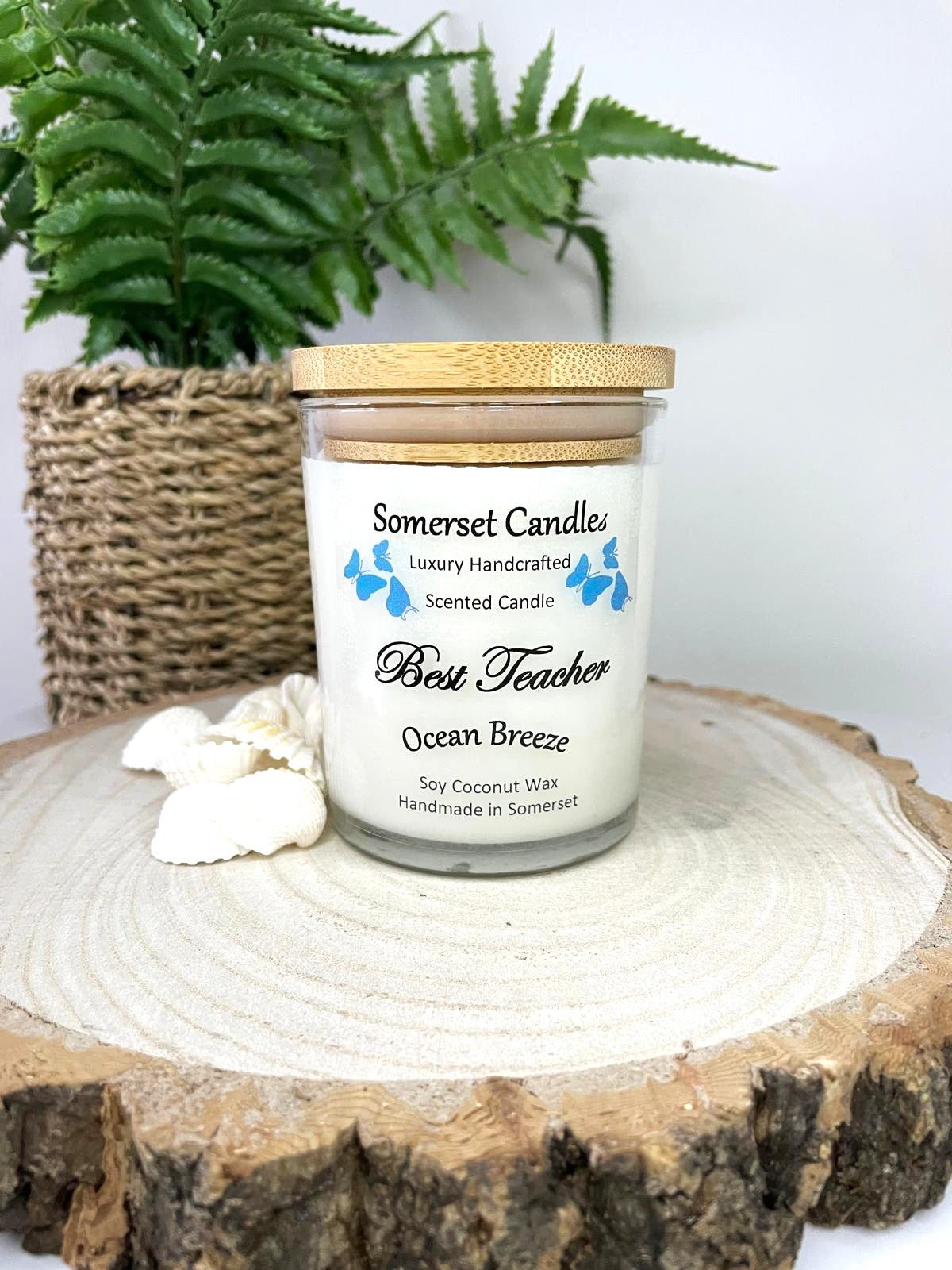White soy candle in a 7oz clear glass jar with a natural wooden lid. The candle is made from a soy-coconut blend and scented with a fresh scent of ocean breeze. Above the scent name on the label, several blue butterflies are displayed, adding a romantic touch. Clean, minimalist design ideal for gifts, home decor or self-care.