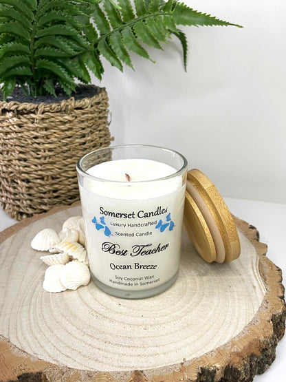 White soy candle in a 7oz clear glass jar with a natural wooden lid. The candle is made from a soy-coconut blend and scented with a fresh scent of ocean breeze. Above the scent name on the label, several blue butterflies are displayed, adding a romantic touch. Clean, minimalist design ideal for gifts, home decor or self-care.