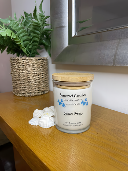 Ocean Breeze scented soy candle displayed on a wooden mantel piece with beautiful white shells. The candle is white in colour with bright blue butterflies fluttering above the scent name and fitted with a lovely bamboo lid.