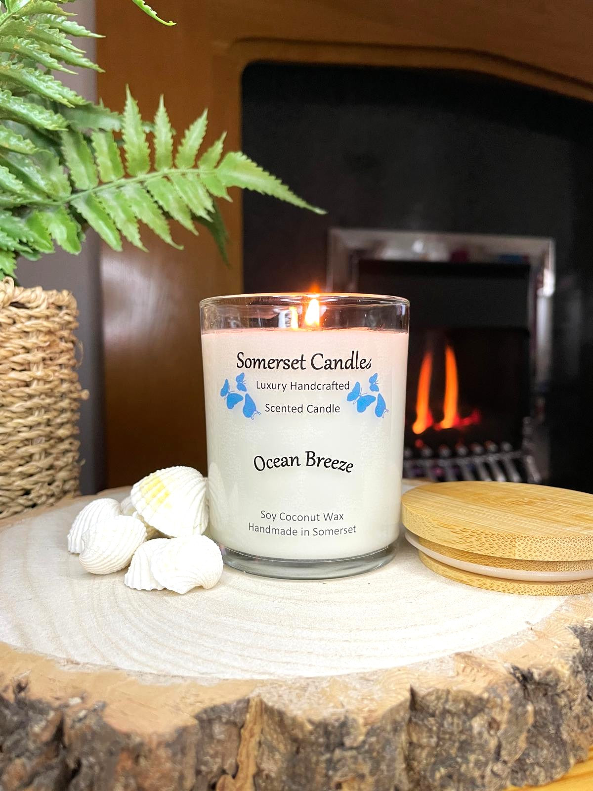 White soy candle in a 7oz clear glass jar with a natural wooden lid. The candle is made from a soy-coconut blend and scented with a fresh scent of ocean breeze. Above the scent name on the label, several blue butterflies are displayed, adding a romantic touch. Clean, minimalist design ideal for gifts, home decor or self-care.