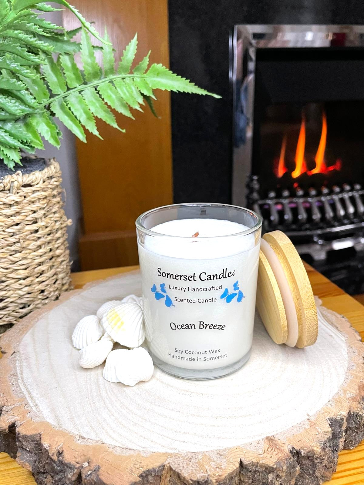 White soy candle in a 7oz clear glass jar with a natural wooden lid. The candle is made from a soy-coconut blend and scented with a fresh scent of ocean breeze. Above the scent name on the label, several blue butterflies are displayed, adding a romantic touch. Clean, minimalist design ideal for gifts, home decor or self-care.