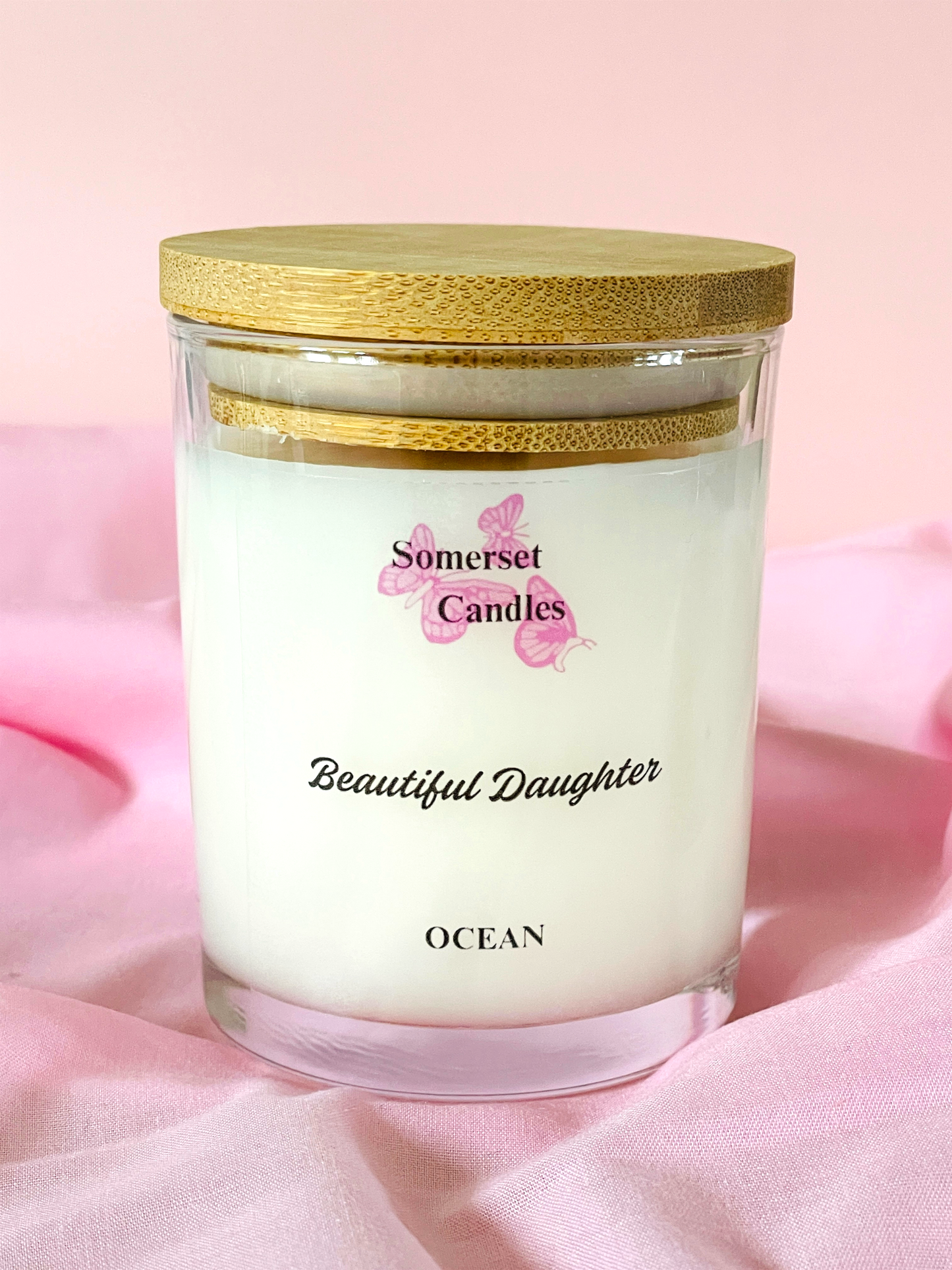 Somerset Candles 'Beautiful Daughter' ocean-scented candle on a pink fabric background