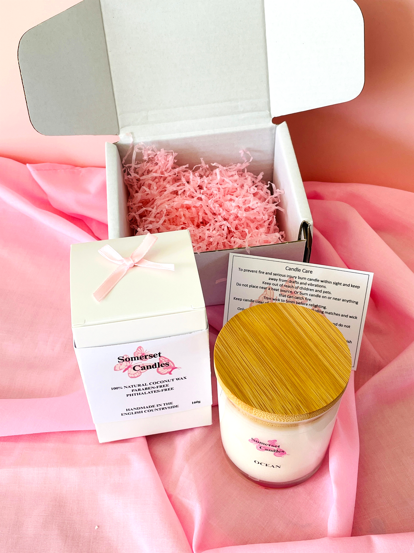 Candle with wooden lid and packaging on a pink fabric background