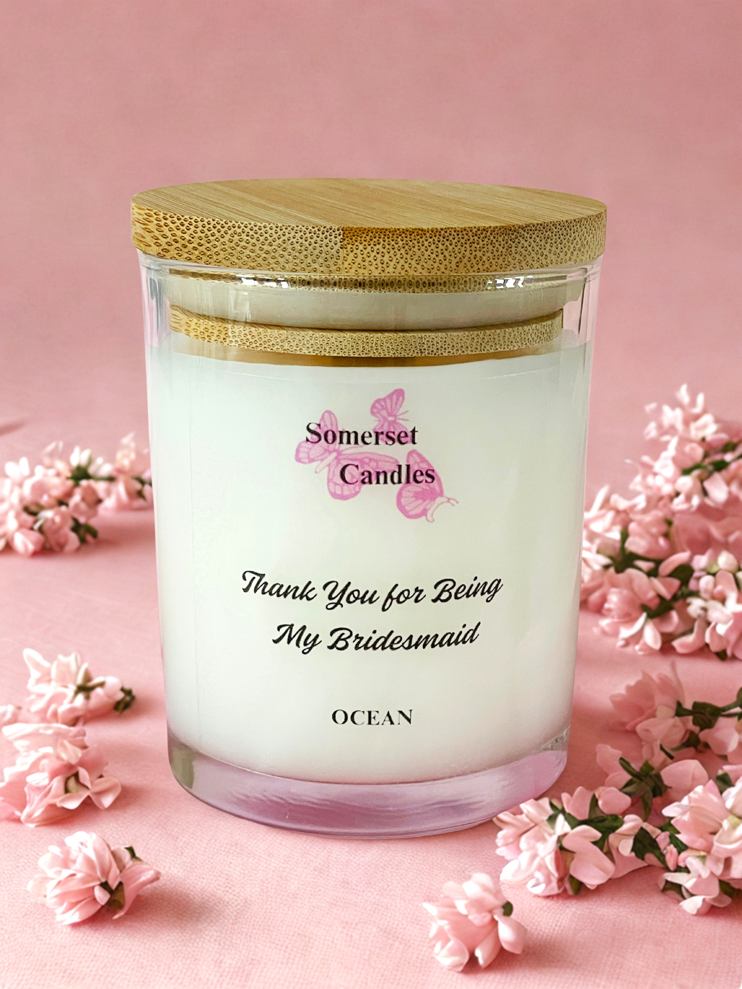 Somerset Candles 'Thank You for Being My Bridesmaid' candle with floral decorations on a pink background