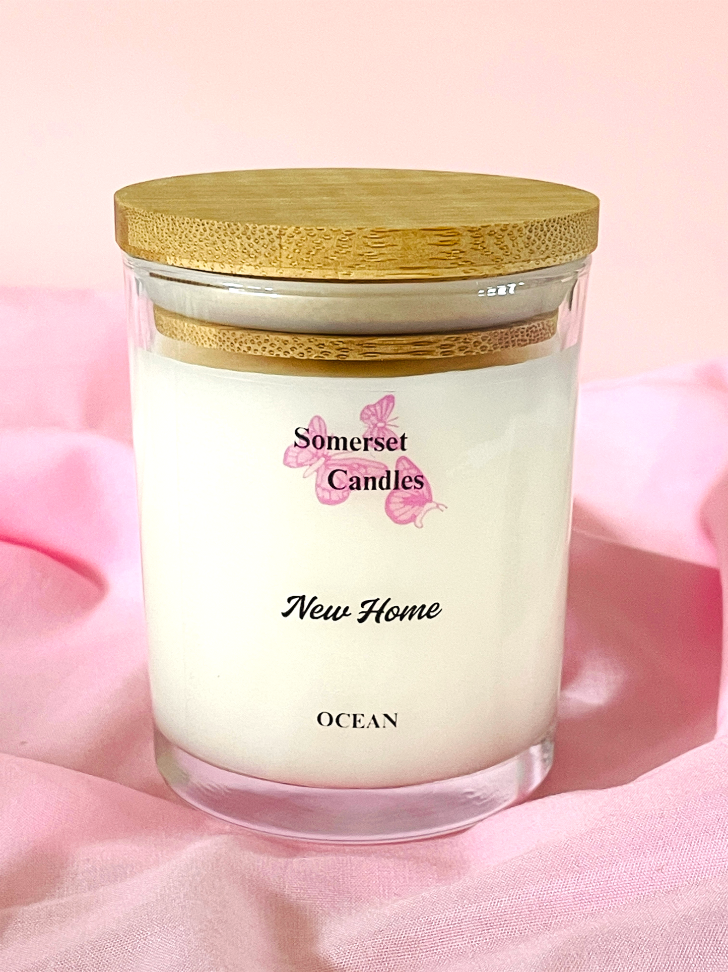 Somerset Candles New Home Ocean candle with wooden lid on a pink fabric background