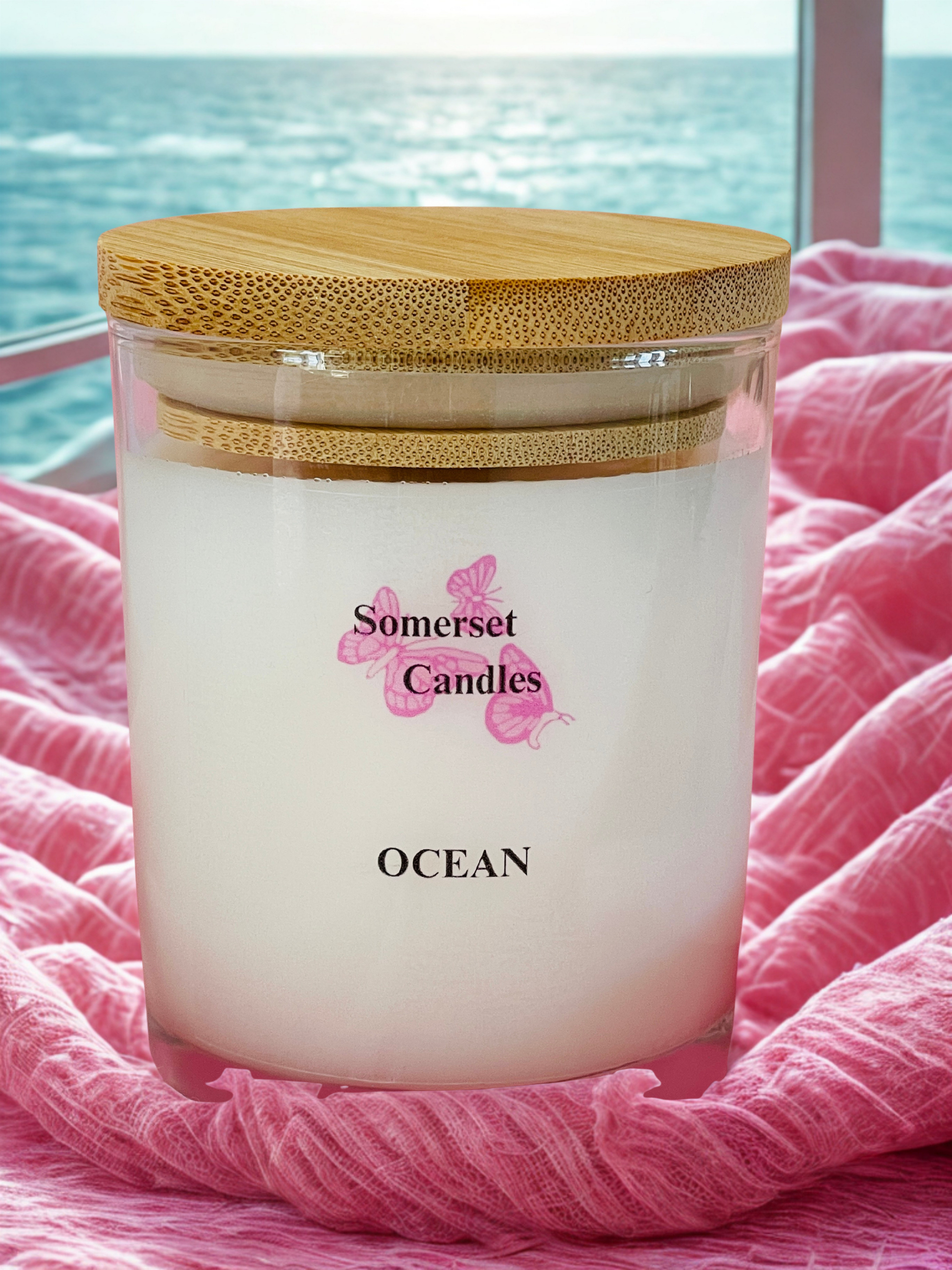 Somerset Candles Ocean scented candle with a wooden lid on pink fabric with ocean view