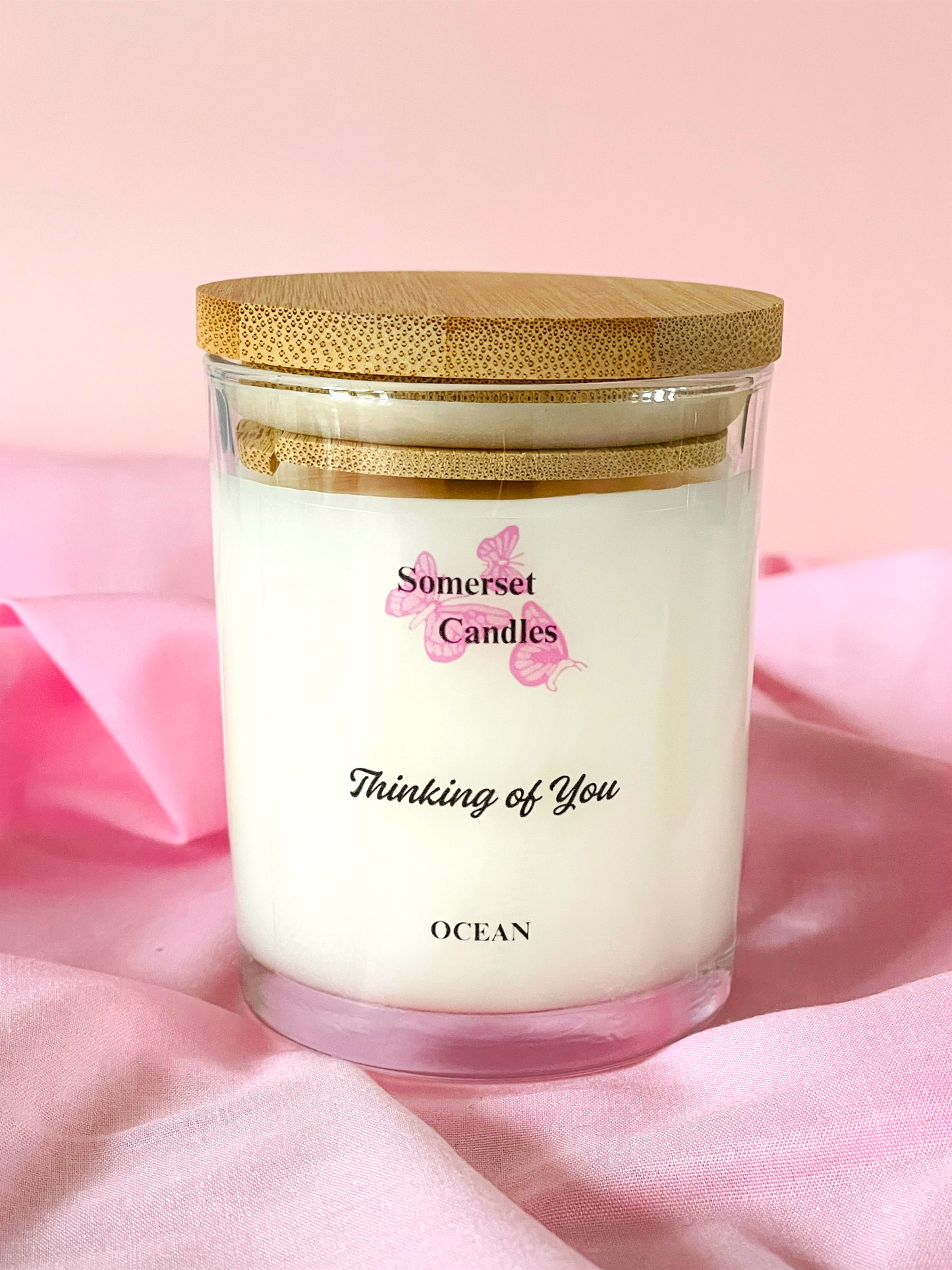 Somerset Candles 'Thinking of You' candle with a wooden lid on a pink fabric background