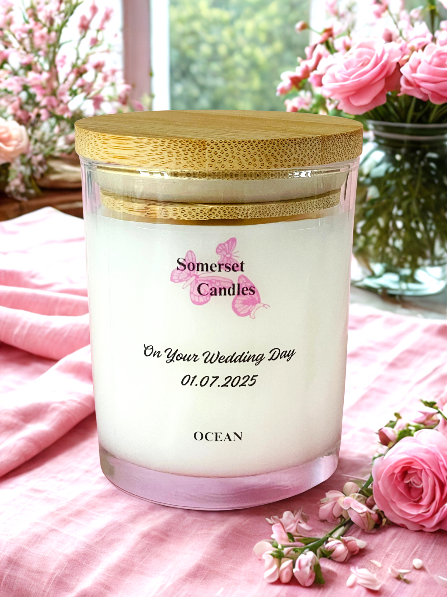 Personalised candle with a wooden lid on a pink fabric background with flowers.