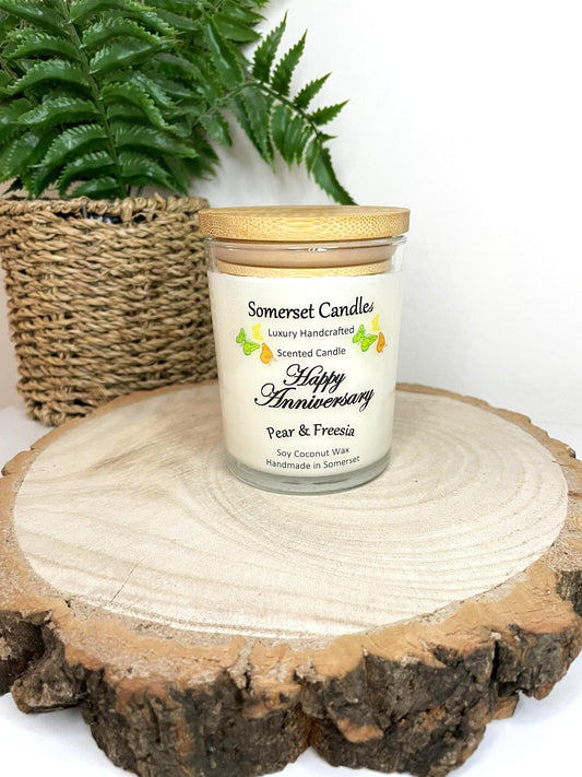 White soy candle in a 7oz clear glass jar with a natural wooden lid. The candle is made from a soy-coconut blend and scented with a delicate fruity floral scent of pear and freesia. Above the scent name on the label, several yellow, green and orange butterflies are displayed, adding a romantic touch. Clean, minimalist design ideal for gifts, home decor or self-care.