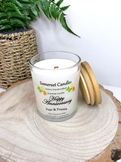 White soy candle in a 7oz clear glass jar with a natural wooden lid. The candle is made from a soy-coconut blend and scented with a delicate fruity floral scent of pear and freesia. Above the scent name on the label, several yellow, green and orange butterflies are displayed, adding a romantic touch. Clean, minimalist design ideal for gifts, home decor or self-care.