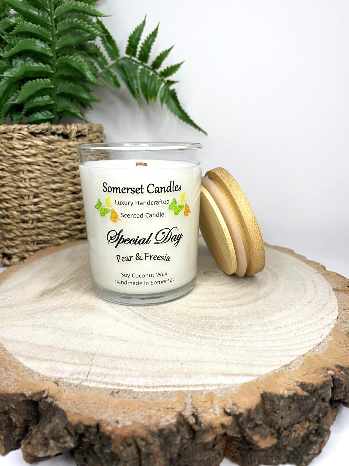 White soy candle in a 7oz clear glass jar with a natural wooden lid. The candle is made from a soy-coconut blend and scented with a delicate fruity floral scent of pear and freesia. Above the scent name on the label, several yellow, green and orange butterflies are displayed, adding a romantic touch. Clean, minimalist design ideal for gifts, home decor or self-care.