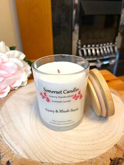 White soy candle in a 7oz clear glass jar with a natural wooden lid. The candle is made from a soy-coconut blend and scented with a soft elegant mix of Peony and Blush Suede. Above the scent name on the label, several pink butterflies are displayed, adding a romantic touch. Clean, minimalist design ideal for gifts, home decor or self-care.