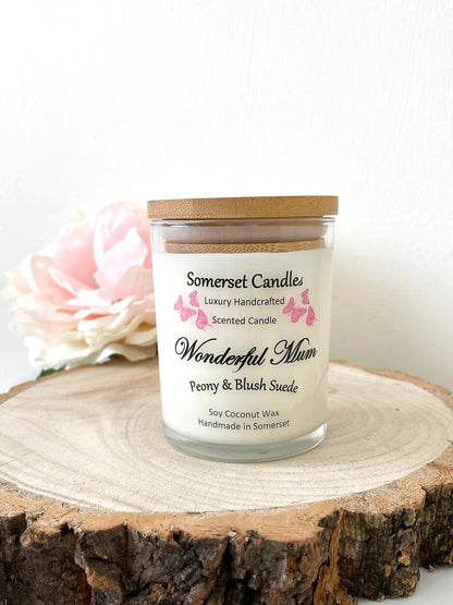 White soy candle in a 7oz clear glass jar with a natural wooden lid. The candle is made from a soy-coconut blend and scented with a delicate mix of peony and blush suede. Above the scent name on the label, several pink butterflies are displayed, adding a romantic touch. Clean, minimalist design ideal for gifts, home decor or self-care.