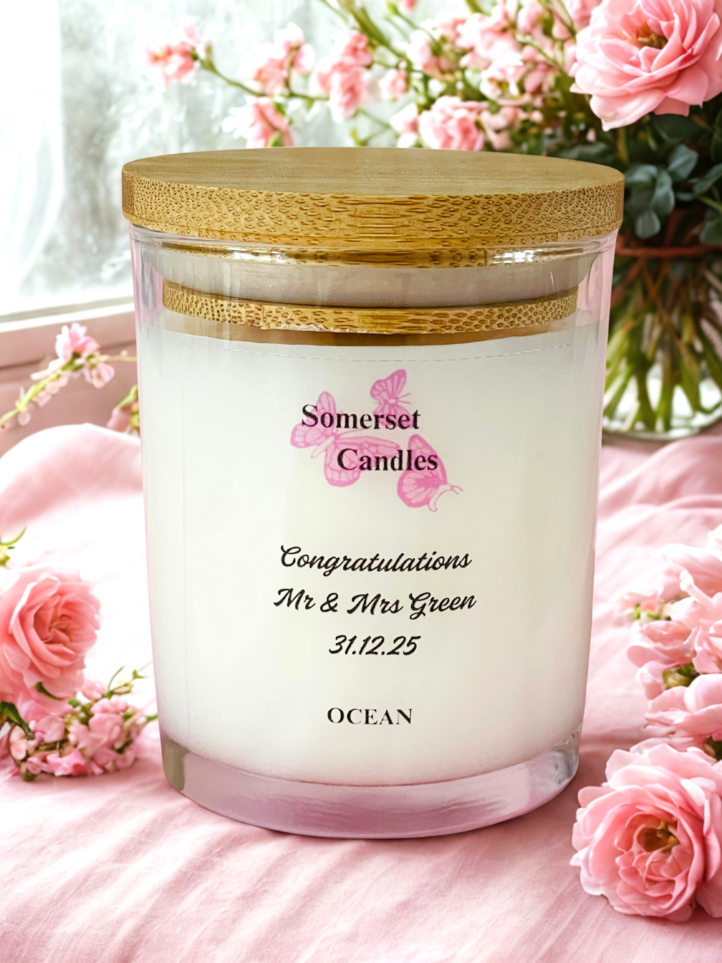 Somerset Candles ocean-scented candle with personalised message surrounded by pink flowers.