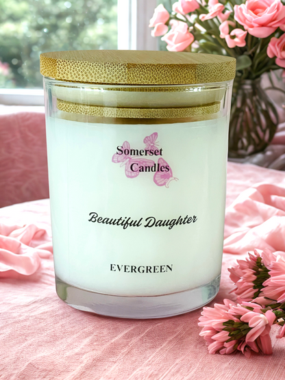 Somerset Candles 'Beautiful Daughter' candle on a pink surface with flowers in the background
