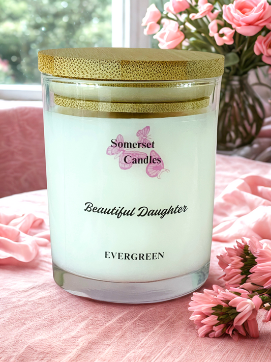 Somerset Candles 'Beautiful Daughter' candle on a pink surface with flowers in the background
