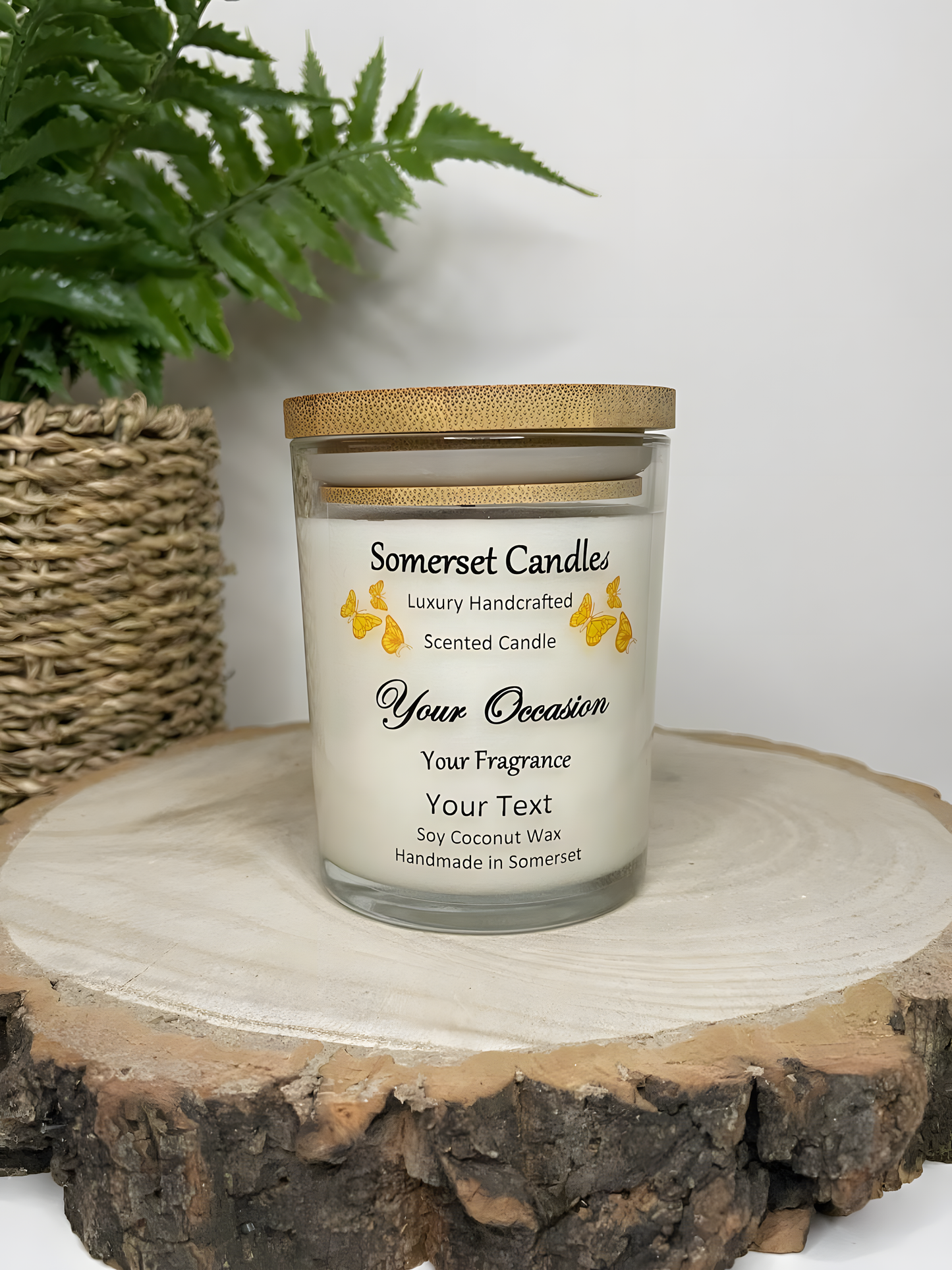 Personalised Scented Soy Candle displayed on a wooden log with a plant behind. The candle is white in colour with orange butterflies above the scent name and a lovely bamboo lid.