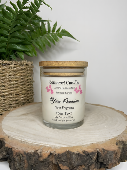 Personalised Scented Soy Candle displayed on a wooden log with a plant behind. The candle is white in colour with pink butterflies above the scent name and a lovely bamboo lid.