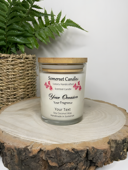 Personalised Scented Soy Candle displayed on a wooden log with a plant behind. The candle is white in colour with red butterflies above the scent name and a lovely bamboo lid.