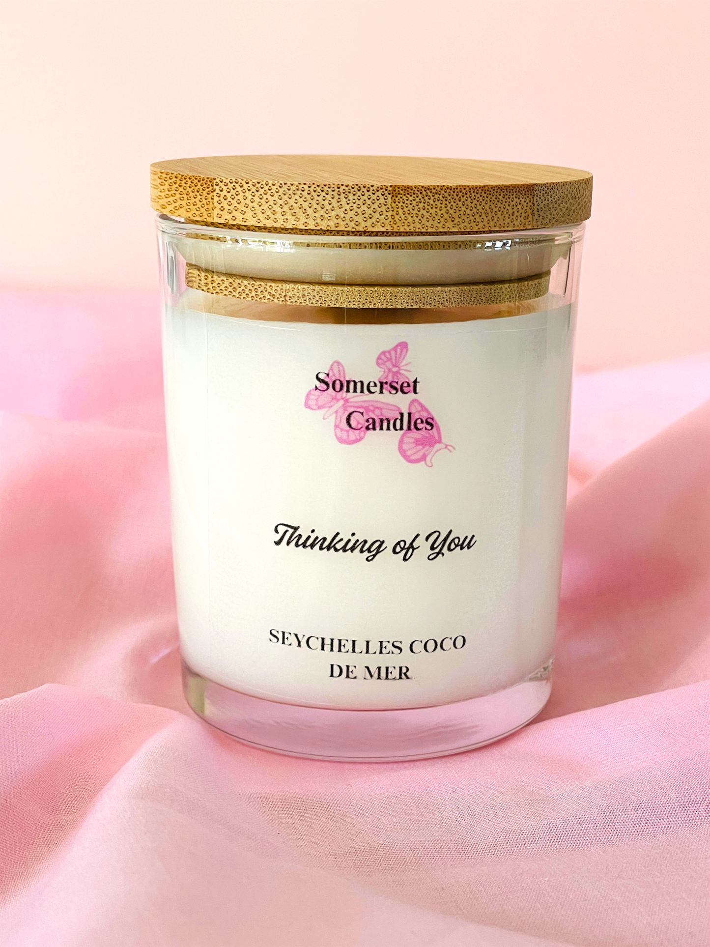 Somerset Candles 'Thinking of You' candle with a gold lid on a pink fabric background