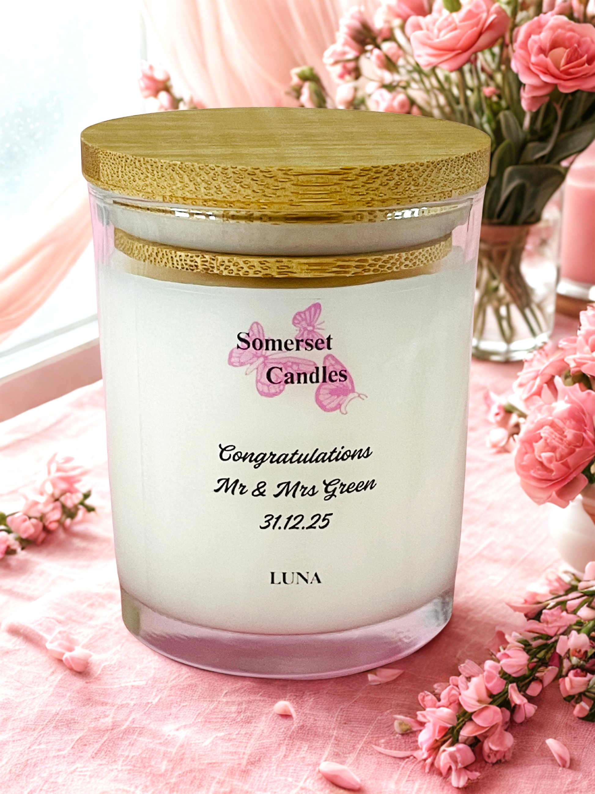 Decorative candle with 'Somerset Candles' branding on a pink surface with flowers.