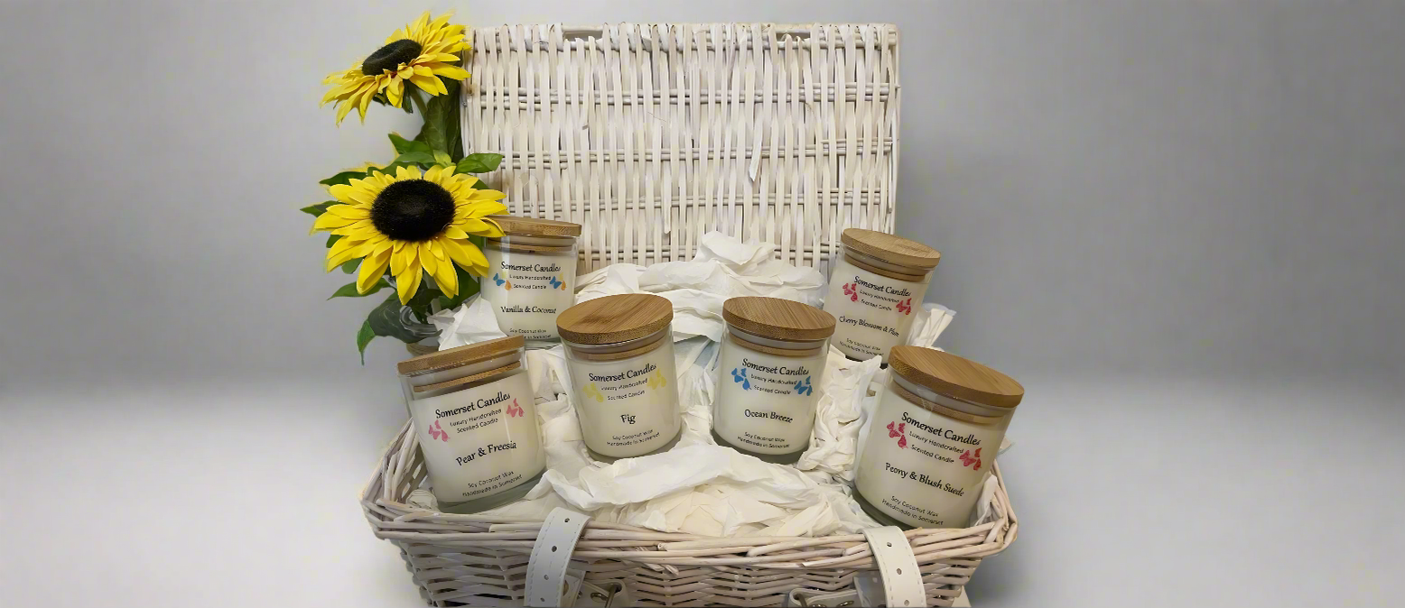 Scented Candles Collection. One of every scented candle arranged in a wicker basket. There are 2 sunflower to the left hand side of the basket.