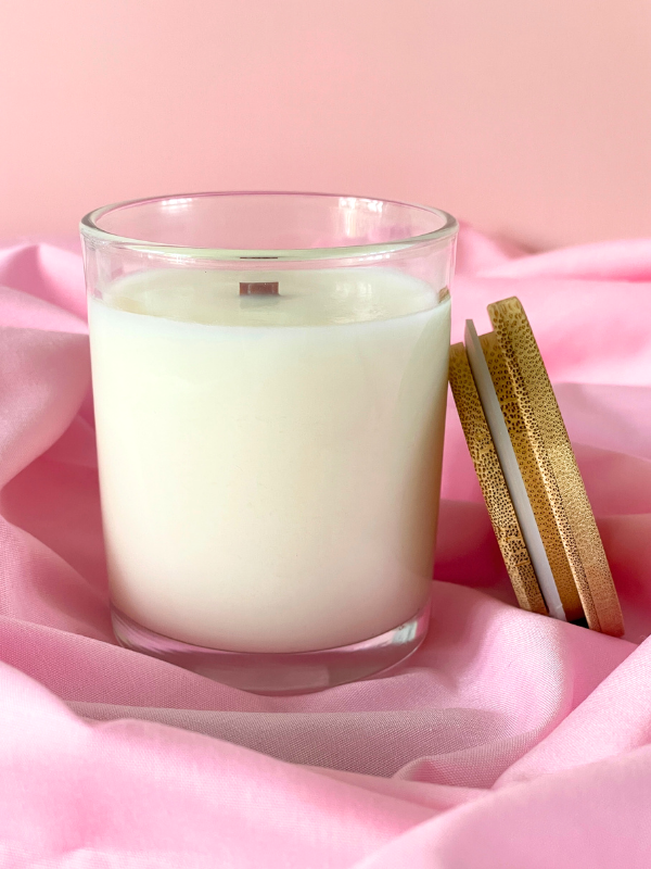 Glass candle with wooden wick on pink fabric background
