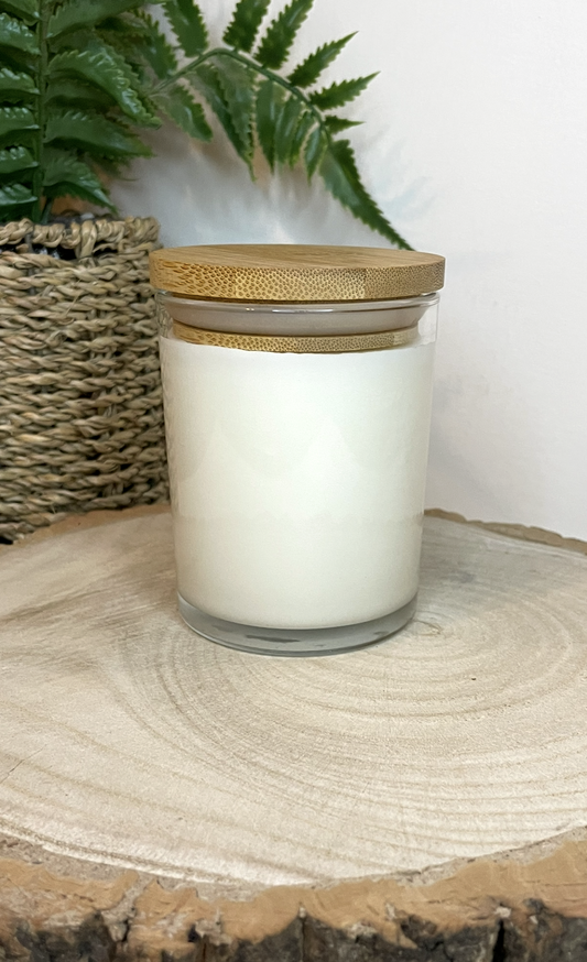 White soy candle in a 7oz clear glass jar with a natural wooden lid. The candle is made from a soy-coconut blend and a variety of fresh fragrances. The candle has no label. Clean, minimalist design ideal for gifts, home decor or self-care.