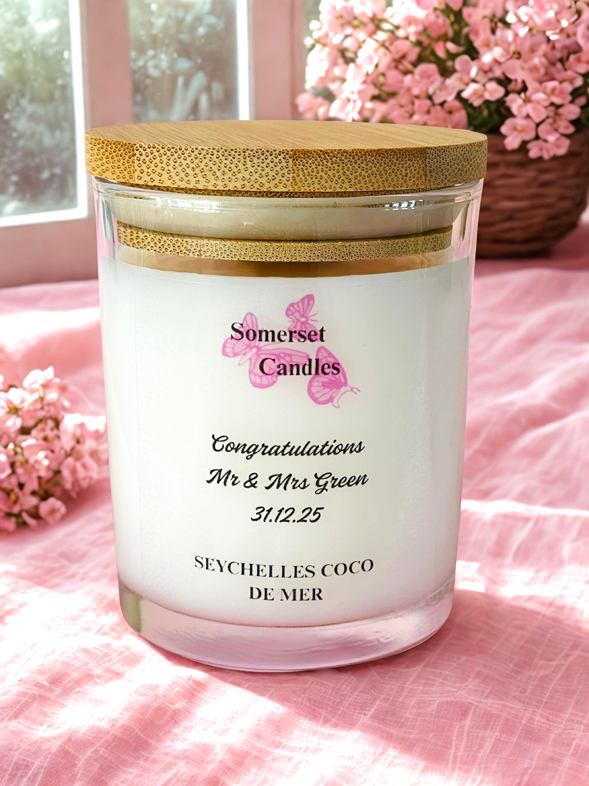 Personalized candle with 'Somerset Candles' branding on a pink surface with flowers.