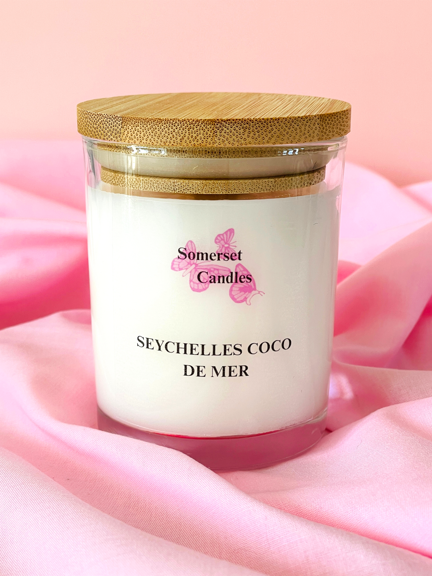 Somerset Candles Seychelles Coco de Mer candle with a wooden lid on a pink fabric background