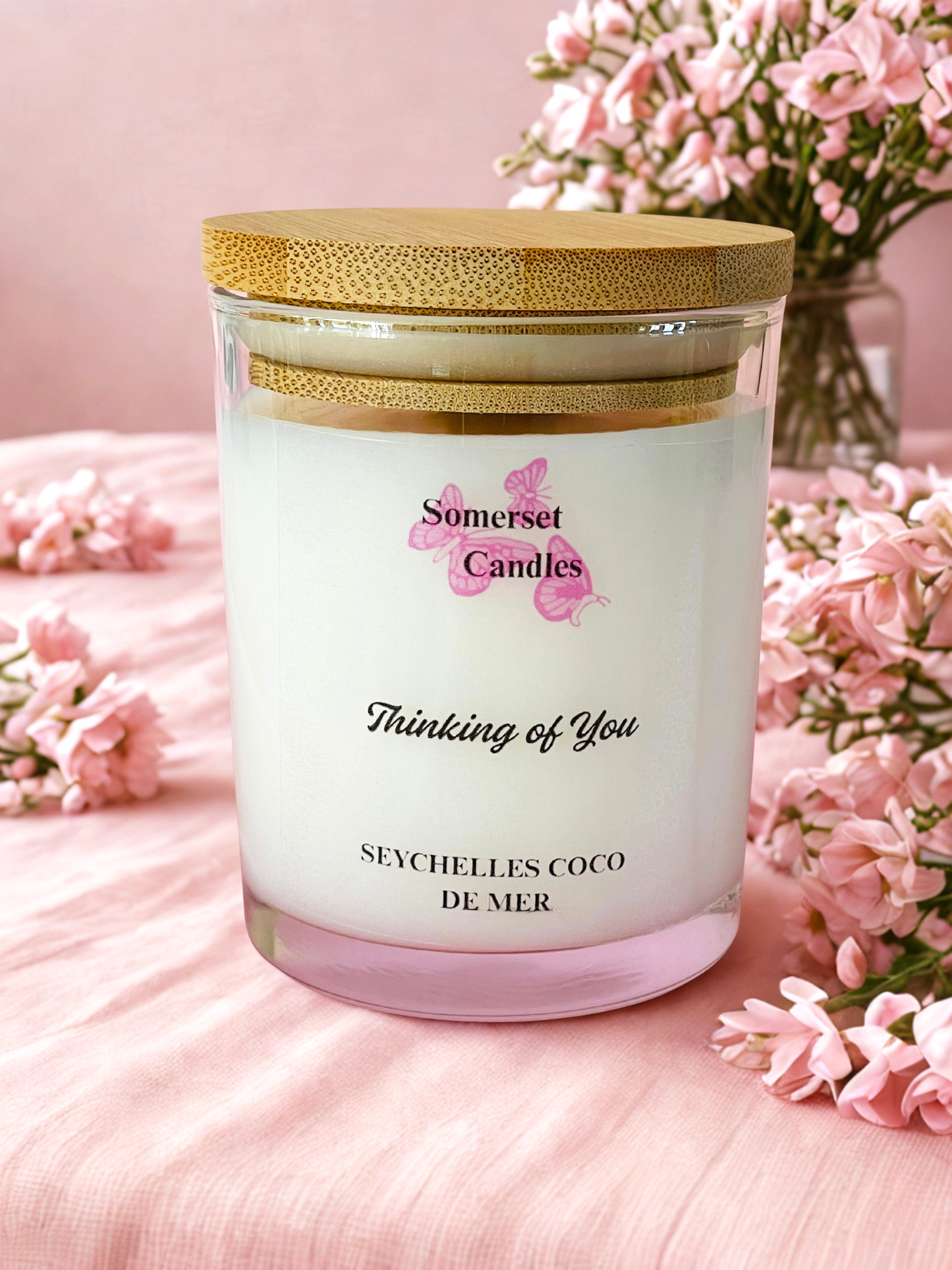 Somerset Candles 'Thinking of You' candle with pink flowers on a pink surface