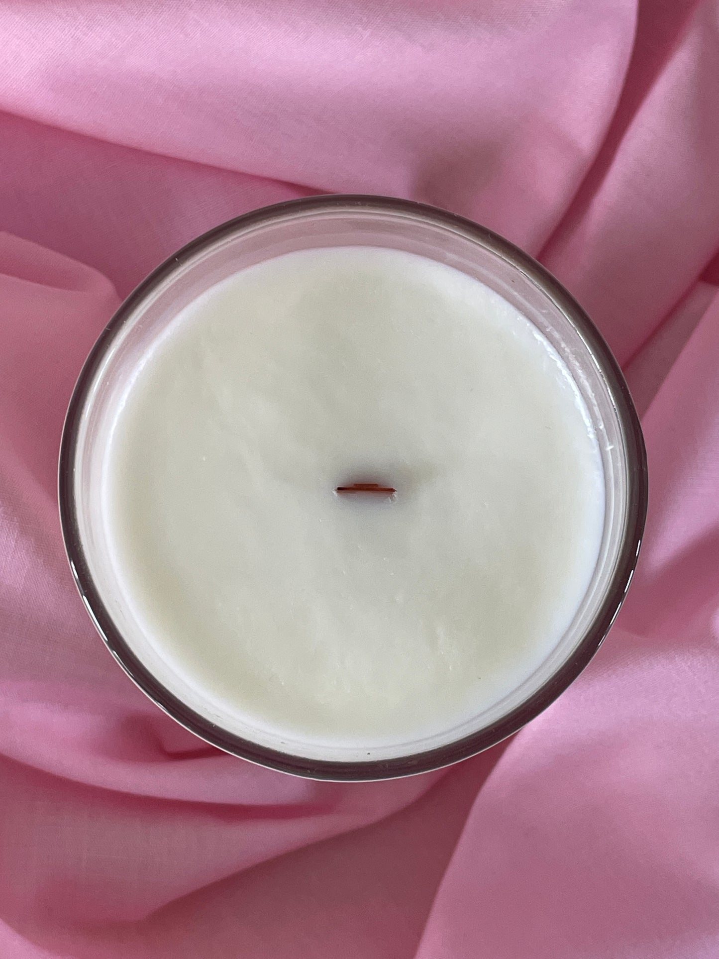 Candle in a glass jar with a wick on a pink fabric background