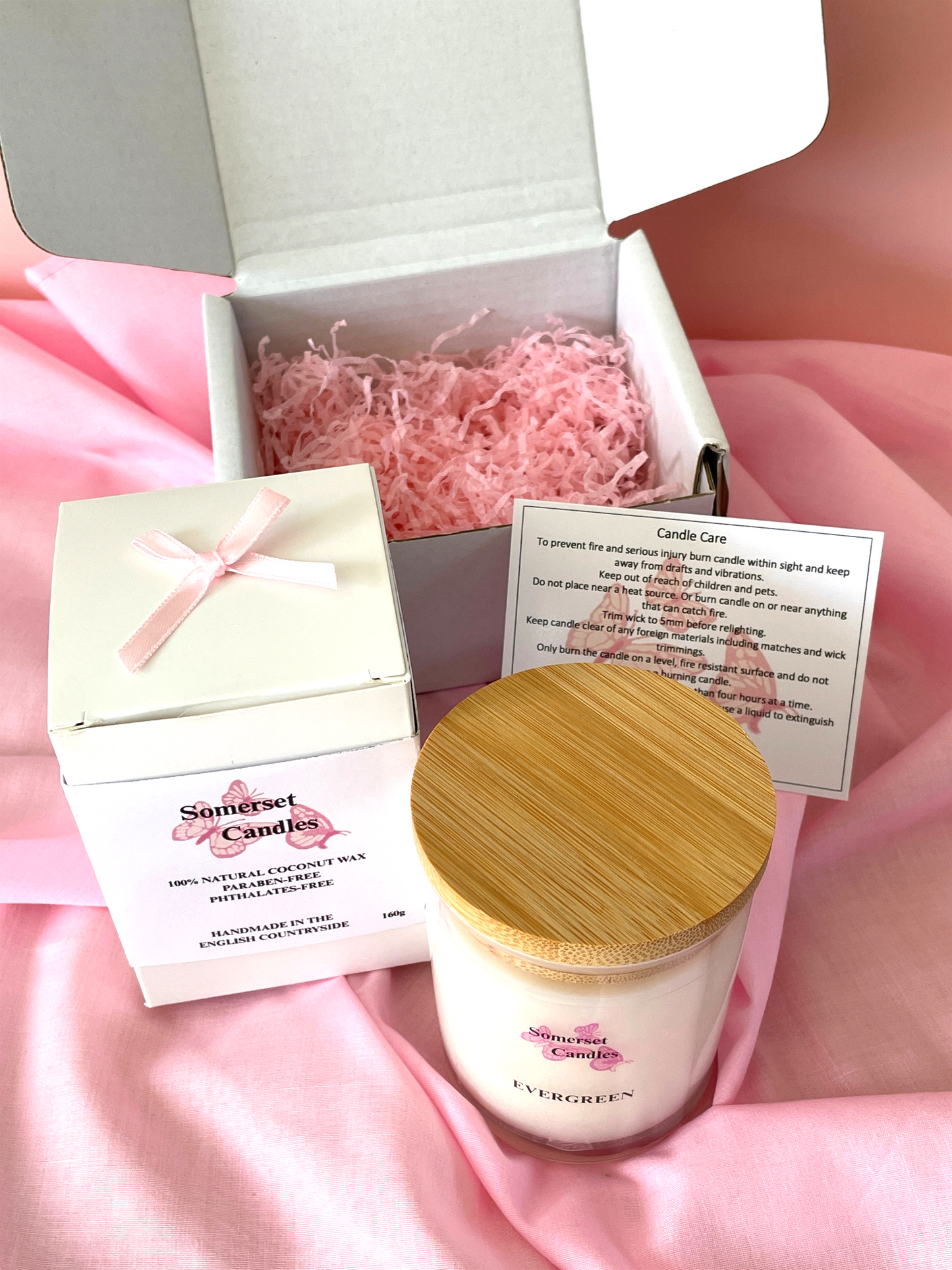 Scented candle with wooden lid and packaging on a pink fabric background