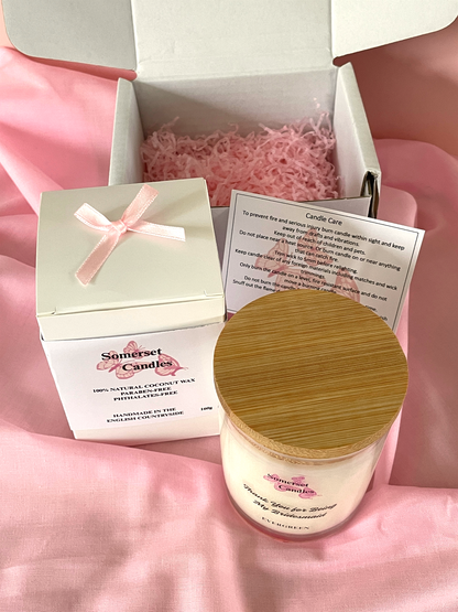 Candle and packaging with a pink ribbon on a pink fabric background