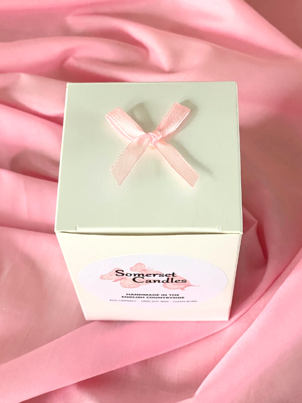 White candle box with pink bow on a pink table cloth