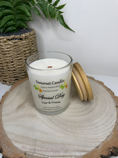 Special Day Pear & Freesia Scented Soy Candle on a wooden board. The candle is white in colour with bright yellow, green & orange butterflies fluttering above the scent name and  with a lovely bamboo lid resting against the glass of the candle.