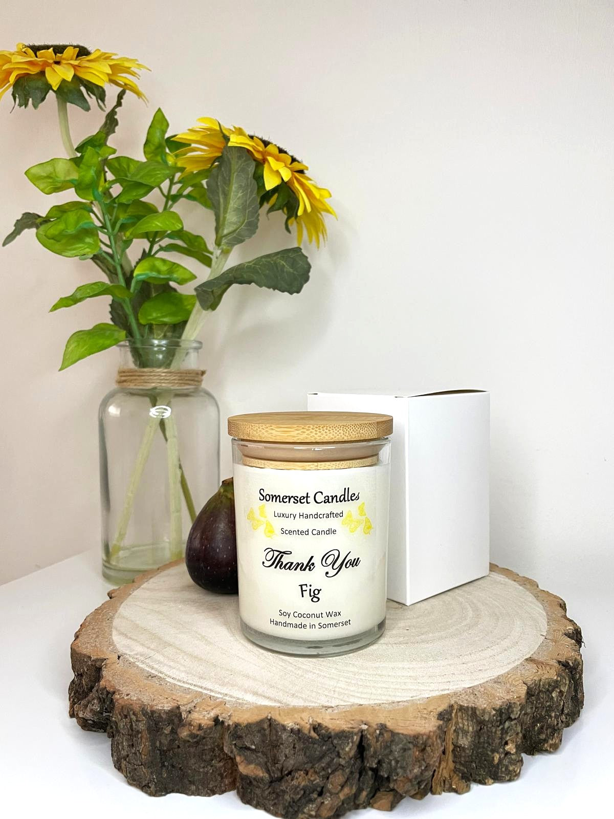 White soy candle in a 7oz clear glass jar with a natural wooden lid. The candle is made from a soy-coconut blend and scented with ripe fig. Above the scent name on the label, several yellow butterflies are displayed, adding a romantic touch. Clean, minimalist design ideal for gifts, home decor or self-care.