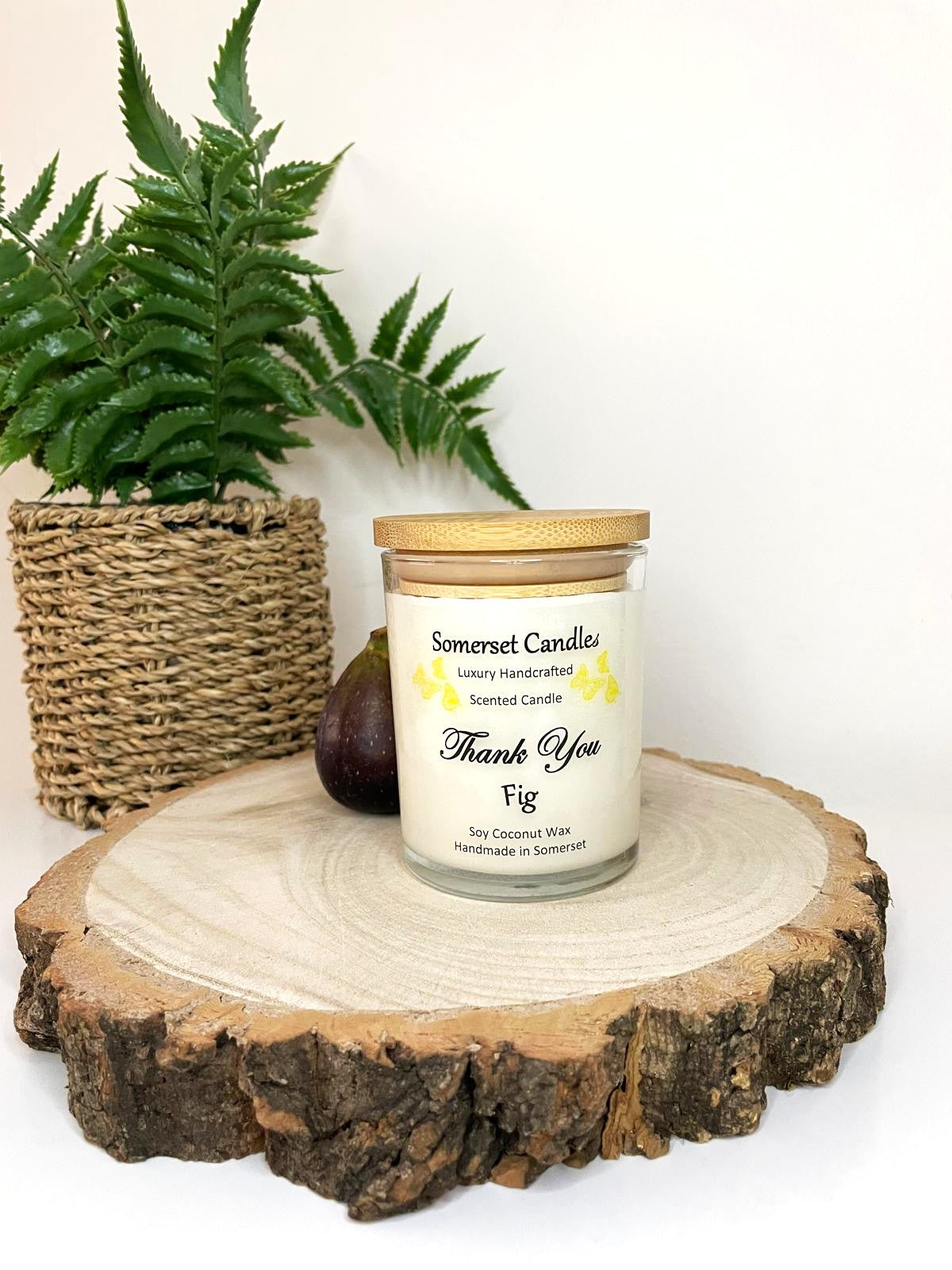 White soy candle in a 7oz clear glass jar with a natural wooden lid. The candle is made from a soy-coconut blend and scented with ripe fig. Above the scent name on the label, several yellow butterflies are displayed, adding a romantic touch. Clean, minimalist design ideal for gifts, home decor or self-care.