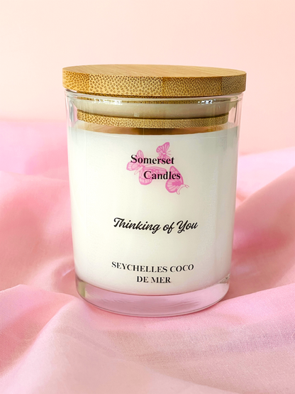 Somerset Candles 'Thinking of You' candle with a gold lid on a pink fabric background