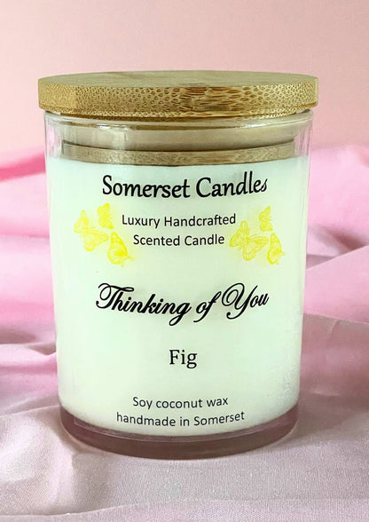 Somerset Candles 'Thinking of You' Fig scented candle with a wooden lid on a pink fabric background.