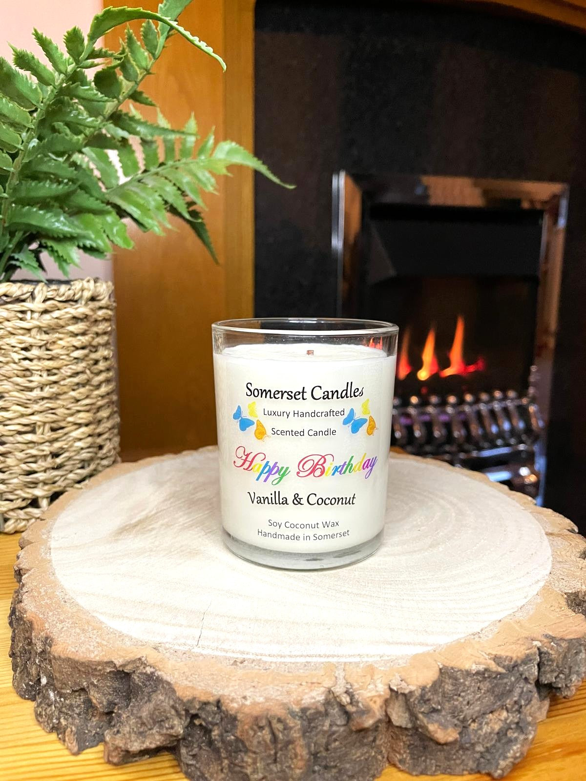 White soy candle in a 7oz clear glass jar with a natural wooden lid. The candle is made from a soy-coconut blend and scented with vanilla and coconut. Above the scent name on the label, several yellow, orange and blue butterflies are displayed, adding a romantic touch. Clean, minimalist design ideal for gifts, home decor or self-care.